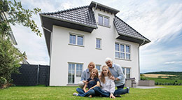 Die Stadtvilla „Vilom“ von Fingerhut Haus Außenansicht der modernen Stadtvilla Vilom von Fingerhut Haus mit markantem Walmdach, Schleppgaube und einer vierköpfigen Familie auf dem Rasen davor.