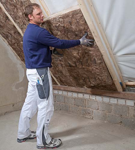 Handwerker verlegt die Zwischensparrendämmung Knauf Insulation aus Glaswolle