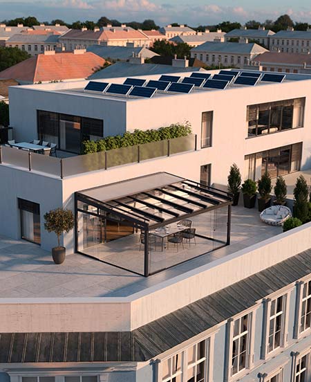 Eine große Penthouse-Dachterrasse mit Photovoltaikanlage auf dem Dach und einer modernen, geschlossenen Glasschiebe-Überdachung über dem Essbereich bei Abendsonne.